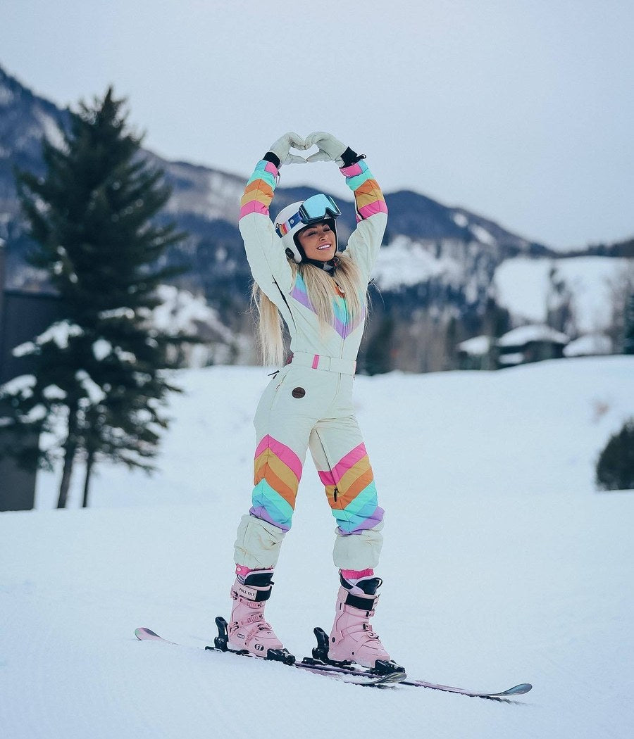 Woman in a rainbow retro one-piece snow suit making a heart on skis