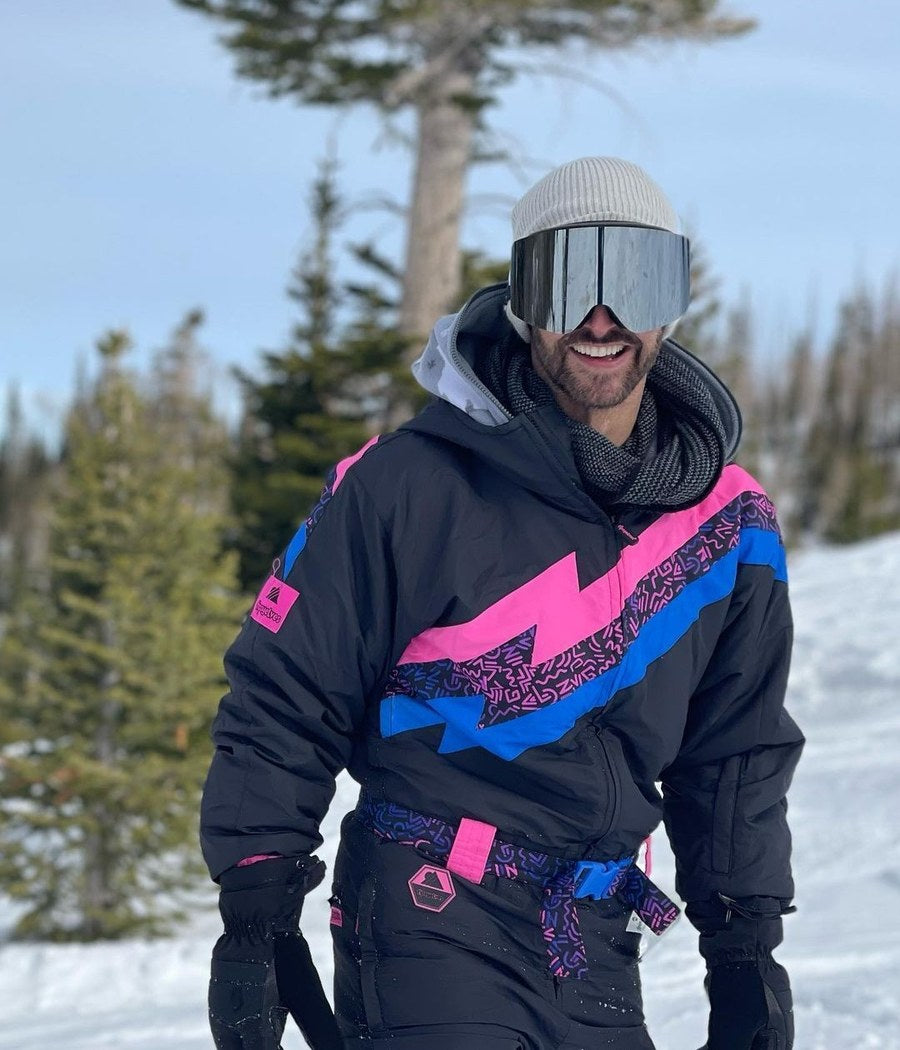 Man in a black retro snow suit with pink and blue lightning bolt on the slopes