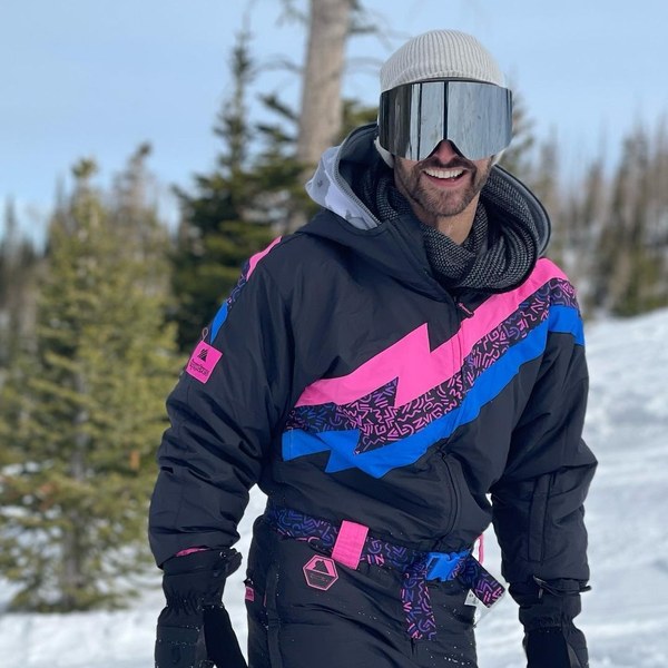 Man in a black retro snow suit with pink and blue lightning bolt on the slopes