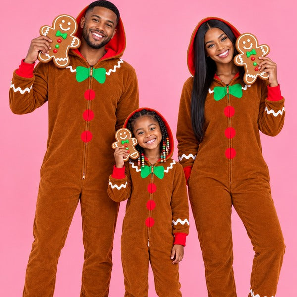 Family in matching gingerbread man jumpsuits holding gingerbread cookies on a pink background